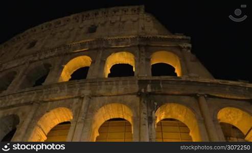Dolly and low angle shot of illuminated Coliseum at night, the world famous ancient amphitheater in Rome, Italy
