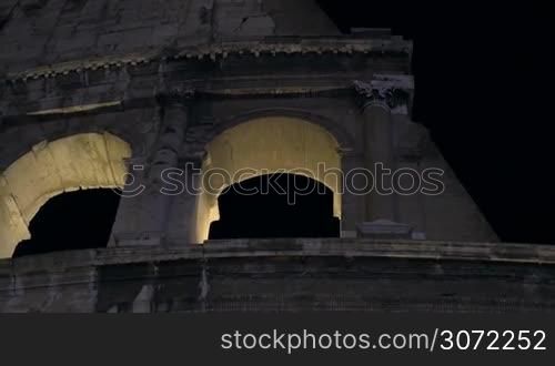 Dolly, close-up and low angle shot of Roman Colosseum illuminated at night. Famous sights of Rome, Italy