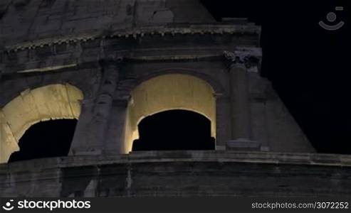 Dolly, close-up and low angle shot of Roman Colosseum illuminated at night. Famous sights of Rome, Italy