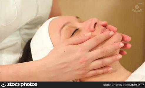 Dolly close-up shot of massage therapist doing a facial massage at beauty treatment salon