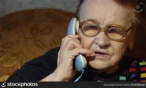 Dolly close-up shot of senior woman in glasses taking a call being at home