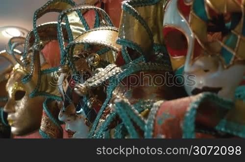 Dolly close-up shot with changing focus of beautiful handmade jester masks exposed in the store. Venetian carnival accessories with colorful and golden decoration