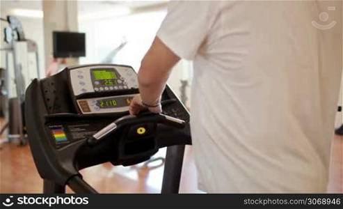 Dolly shot of a man walking on the treadmil and changing setting on electronic board