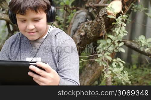 Dolly shot of a teenager in headphones using tablet computer outdoor