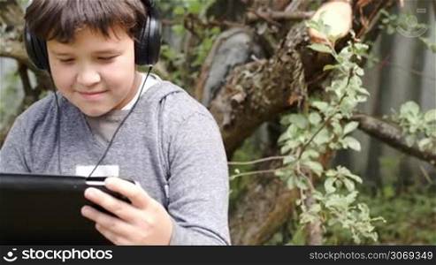 Dolly shot of a teenager in headphones using tablet computer outdoor