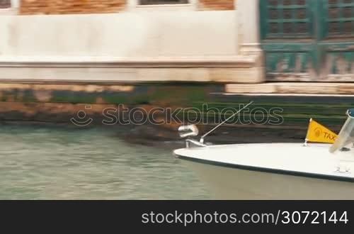Dolly shot of a woman sitting by the canal in Venice and using laptop, two boats sailing by