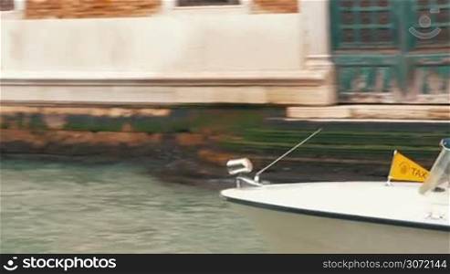 Dolly shot of a woman sitting by the canal in Venice and using laptop, two boats sailing by