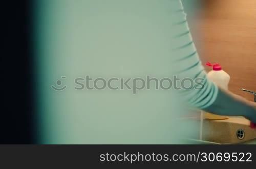 Dolly shot of a woman washing the dishes in the kitchen at home in the evening