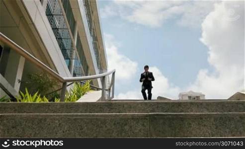 Dolly shot of a young and happy chinese businessman sliding downstairs on rails of office staircase. The man enjoys his new promotion at job