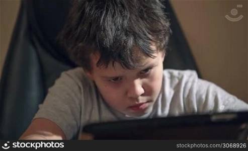 Dolly shot of boy busy with tablet PC sitting at the table