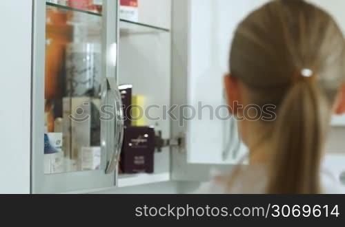 Dolly shot of cosmetician taking cosmetic from cabinet and showing it her colleague