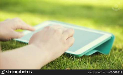 Dolly shot of female hands typing on Tablet PC on grass
