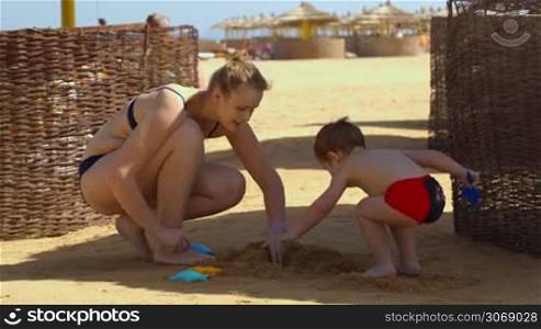 Dolly shot of happy mother and her child playing on the beach during summer vacation
