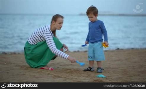 Dolly shot of happy mother and son playing with toys on the beach