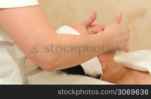 Dolly shot of massage therapist providing a seance of facial massage at beauty spa