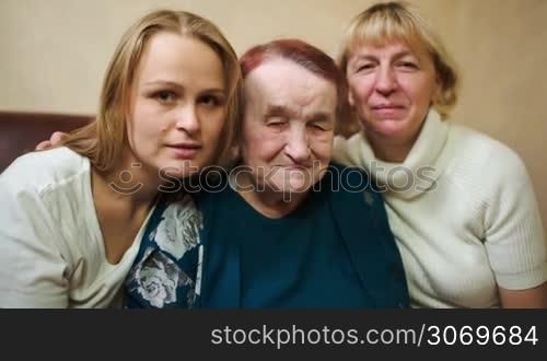 Dolly shot of three women as symbol of three generations. Smiling daughter, mother and grandmother looking to the camera