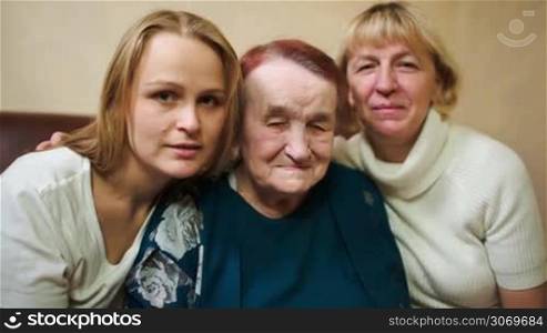 Dolly shot of three women as symbol of three generations. Smiling daughter, mother and grandmother looking to the camera