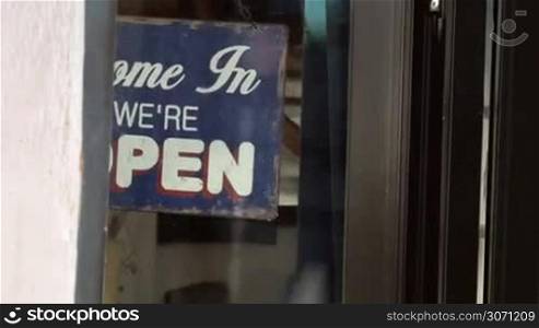 Dolly shot of woman closing the glass door and turning over vintage style shop-sign from open to closed