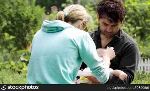Dolly shot of young parents feeding their baby outdoor on a bright summer day