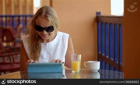 Dolly shot of young woman on cafe terrace using laptop, drinking fresh juice and enjoying outside view