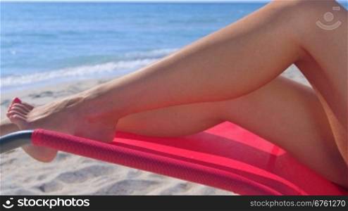Dolly: Tanned female legs in lounge chair on summer sandy beach