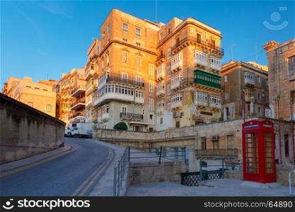 Domes and roofs at sunset, Valletta , Malta. The traditional Maltese street with red phone box and building with colorful shutters and balconies at sunrise, Valletta, Capital city of Malta