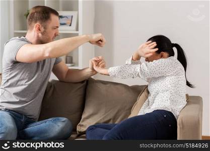 domestic violence, abuse and people concept - couple having fight and man beating helpless woman at home. unhappy woman suffering from home violence