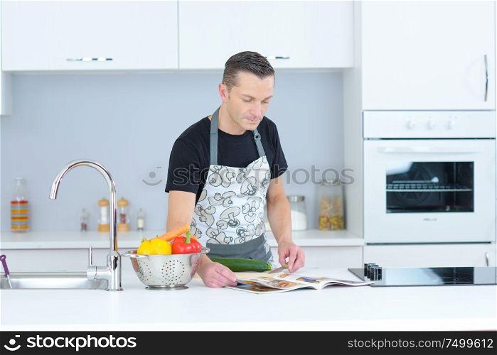 domesticated man in kitchen looking through recipe magazine