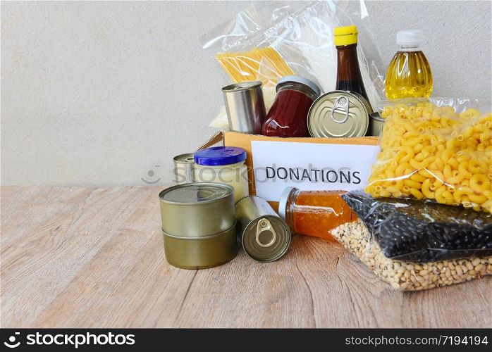 Donations box with canned food on wooden table background / pasta canned goods and dry food non perishable with pea cooking oil rice noodles spaghetti macaroni donations food concept