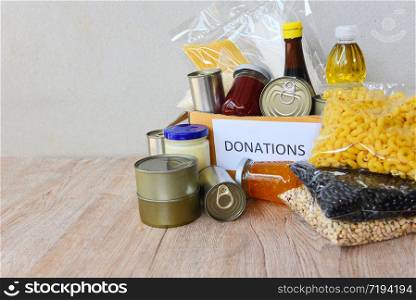 Donations box with canned food on wooden table background / pasta canned goods and dry food non perishable with pea cooking oil rice noodles spaghetti macaroni donations food concept