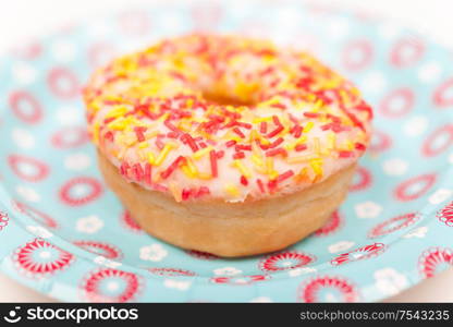 Donut or doughnut with colorful frosting or icing and sprinkles photographed on a party plate