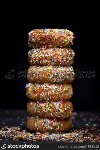 donuts mountain with strawberry syrup and coloured topping on a black background
