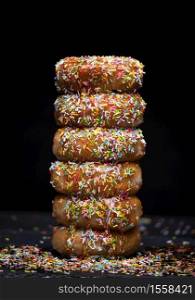 donuts mountain with strawberry syrup and coloured topping on a black background