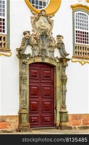 Door of an old church in baroque style with carved stone frame and decorated with images and symbols in the historic city of Tiradentes in Minas Gerais, Brazil. Old baroque church door in Tiradentes