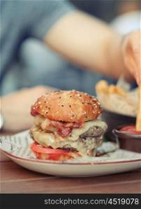 Double cheeseburger on table in outdoor restaurant with shallow depth of field. Blurred young man in background.