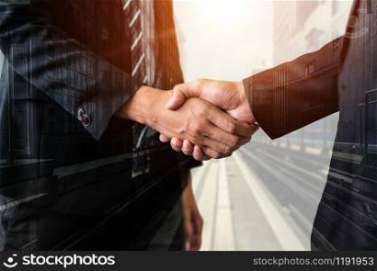 Double exposure image of business people handshake on city office building in background showing partnership success of business deal. Concept of corporate teamwork, trust partner and work agreement.