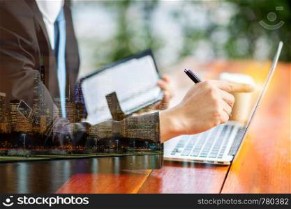 Double exposure of businessman hand with laptop and skyline building background