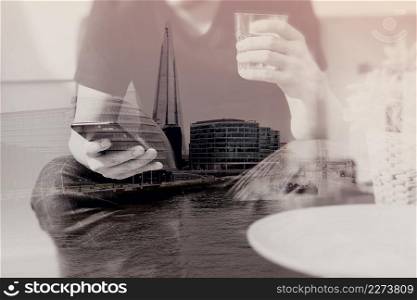 double exposure of designer man hand with glass of water using smart phon for mobile payments online shopping,omni channel,vase rattan with plant and wooden tray on table,London architecture city