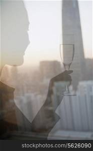 Double exposure of woman toasting with champagne flute over cityscape