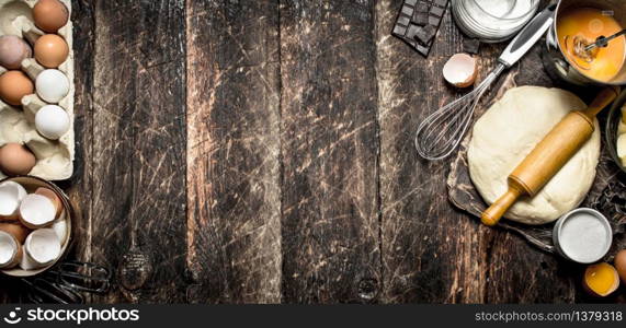 Dough background. The pastry with a rolling pin and ingredients. On a wooden table.