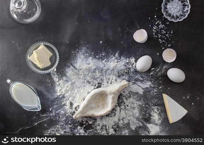 Dough on black table with flour and ingridients. Top view, khachapuri cooking