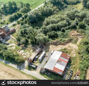 Downsized plant for the repair of machines with a scrap yard behind a forest with a wild dump, diagonally shot aerial photograph, made with drone