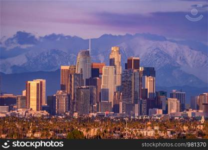 Downtown Los Angeles skyline with snow capped mountains behind at sunset