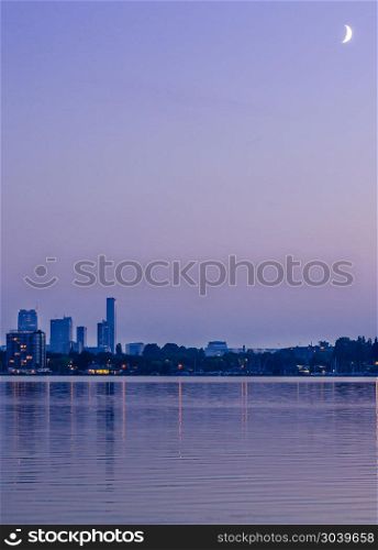 Downtown Rotterdam, Netherlands at blue hour with a crescent moon, captured from the lake at Kralingen Park in the East part of the city. Downtown Rotterdam, Netherlands at blue hour with a crescent moon, captured from the lake at Kralingen Park in the East part of the city.