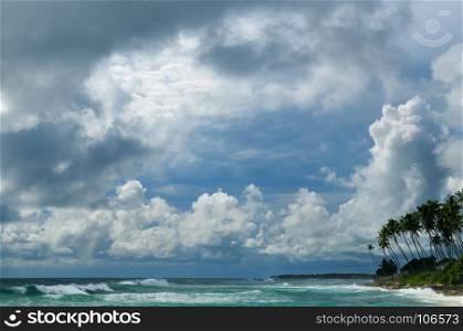 Dramatic cloudscape with heavy rain and tropical storm at the horizon on the coastline of Sri Lanka. Wide angle shot frome the sandy beach.