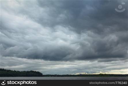 Dramatic dark stormy sky with huge heavy rain clouds before a thunderstorm. Lake Seliger, Russia. Atmospheric natural background with space for copy, selective focus.
