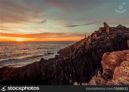 Dramatic horizontal shot of a white lighthouse during the sunset from the rocks of the coast