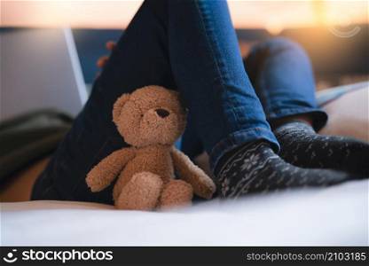 Dramatic Lonely teddy bear lying on kid legs with sunlight shining from window, Sad brown bare lying in bed with in morning,Fluffy plush toy with blurry background.International missing children&rsquo;s day