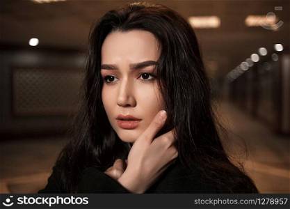 dramatic portrait of a beautiful young woman in a black coat in an underground passage.mosaics on the walls are not someone&rsquo;s works of art.these are walls in an underground passage in Eastern style