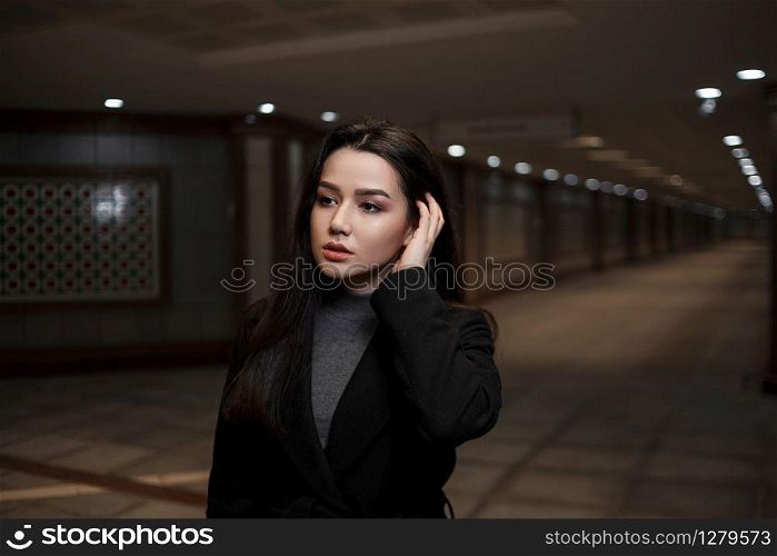 dramatic portrait of a beautiful young woman in a black coat in an underground passage.mosaics on the walls are not someone&rsquo;s works of art.these are walls in an underground passage in the Eastern style